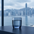 Vaso de agua en el borde de un escritorio con el skyline de Hong Kong desenfocado al fondo